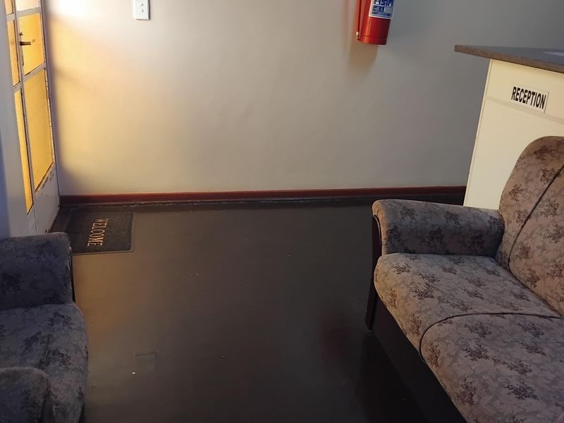 An entrance area featuring a reception counter, fire safety equipment, and dark flooring, providing a functional welcome space for the property.