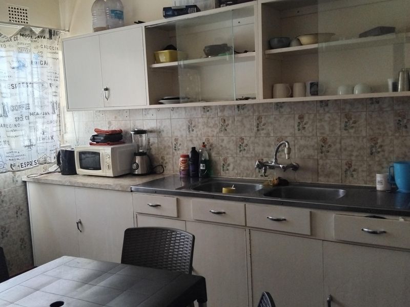A functional kitchen featuring dated cabinetry, a double stainless steel sink, and tiled backsplash, offering potential for modernization and aesthetic updates.