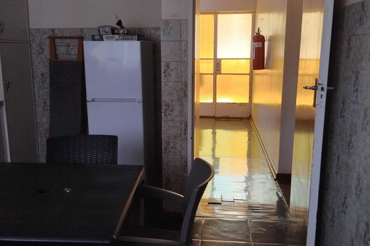A dated kitchen area featuring tiled walls and flooring, with a doorway leading to an adjacent hallway area.