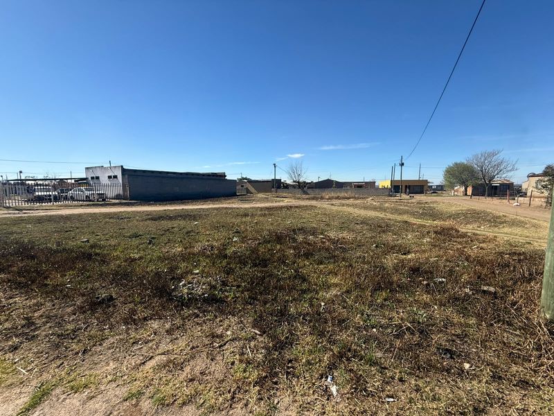 A vacant residential plot of land featuring open ground, perimeter fencing, and surrounding neighborhood infrastructure.