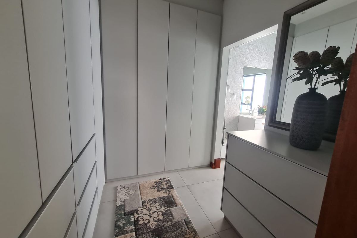 A modern dressing area featuring extensive floor-to-ceiling built-in cupboards and neutral tiled flooring, leading into an adjoining bathroom space.