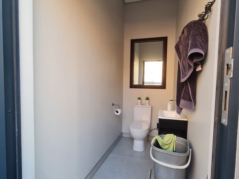 A compact guest bathroom featuring a modern toilet, vanity with basin, and wall-mounted mirror, finished with neutral wall tones and tiled flooring.