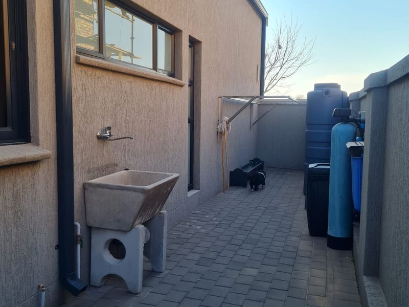 A paved side utility area featuring a concrete sink, water filtration system, and storage tank against the exterior wall of the house.