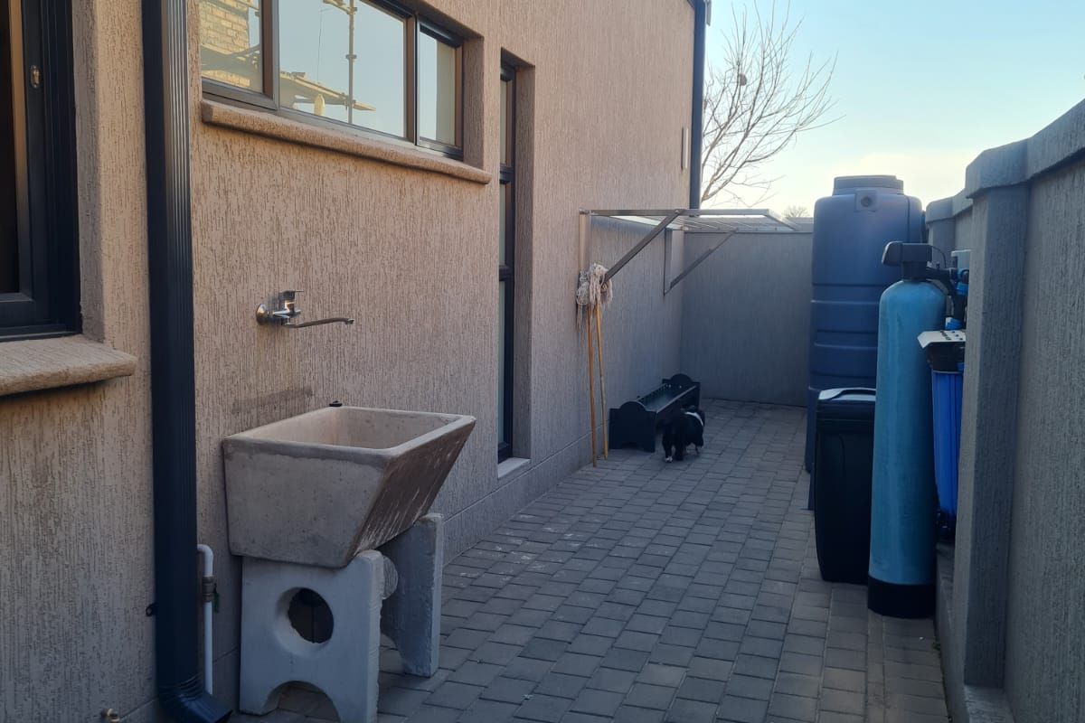 A paved side utility area featuring a concrete sink, water filtration system, and storage tank against the exterior wall of the house.