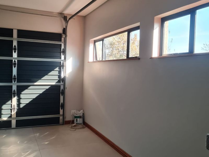 A clean, empty garage space featuring tiled flooring, a sectional garage door, and natural light through side windows.