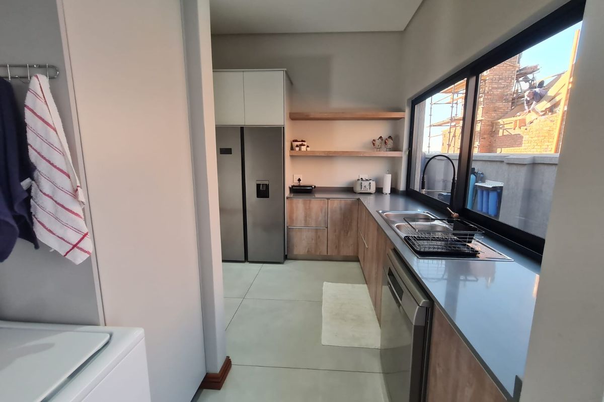 Modern kitchen featuring sleek cabinetry, stone countertops, floating timber shelving, and a large window providing ample natural light.