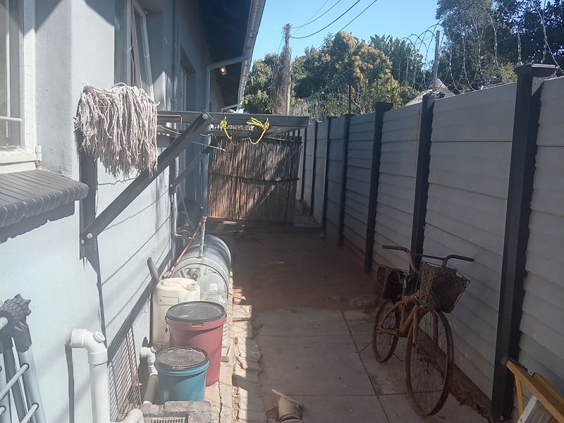 A narrow rear exterior walkway featuring a precast concrete boundary wall with razor wire, external geyser, and paved flooring.