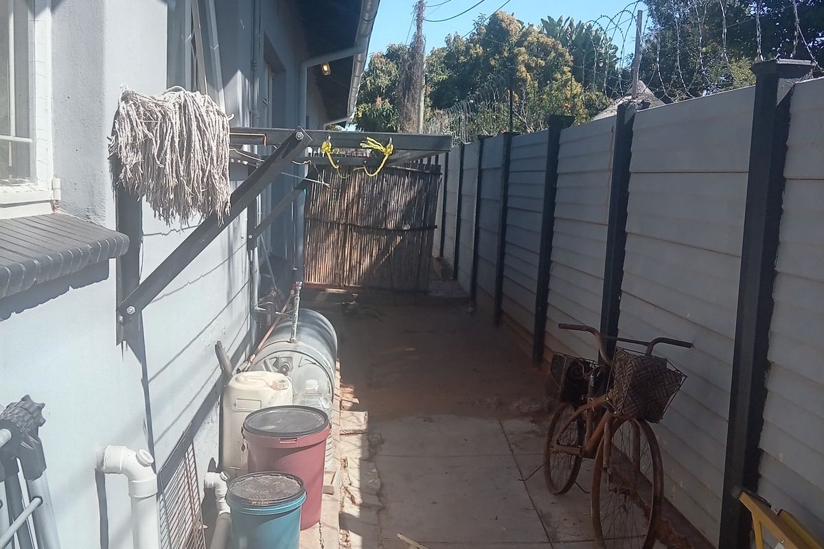 A narrow rear exterior walkway featuring a precast concrete boundary wall with razor wire, external geyser, and paved flooring.