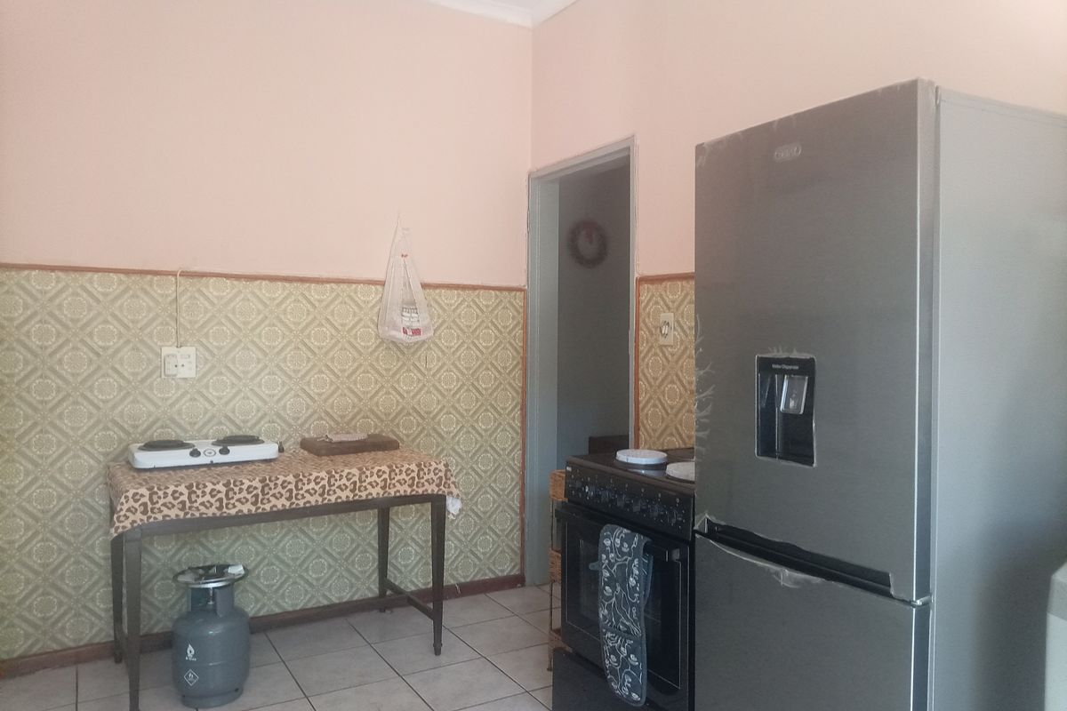 A functional kitchen area featuring tiled flooring and patterned wallpaper, equipped with a freestanding oven and ample space for food preparation.