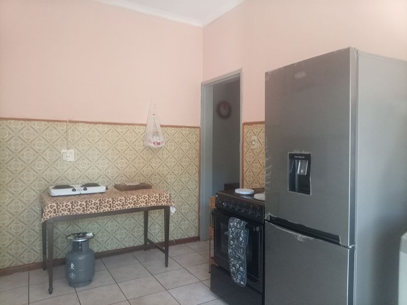 A functional kitchen area featuring tiled flooring and patterned wallpaper, equipped with a freestanding oven and ample space for food preparation.