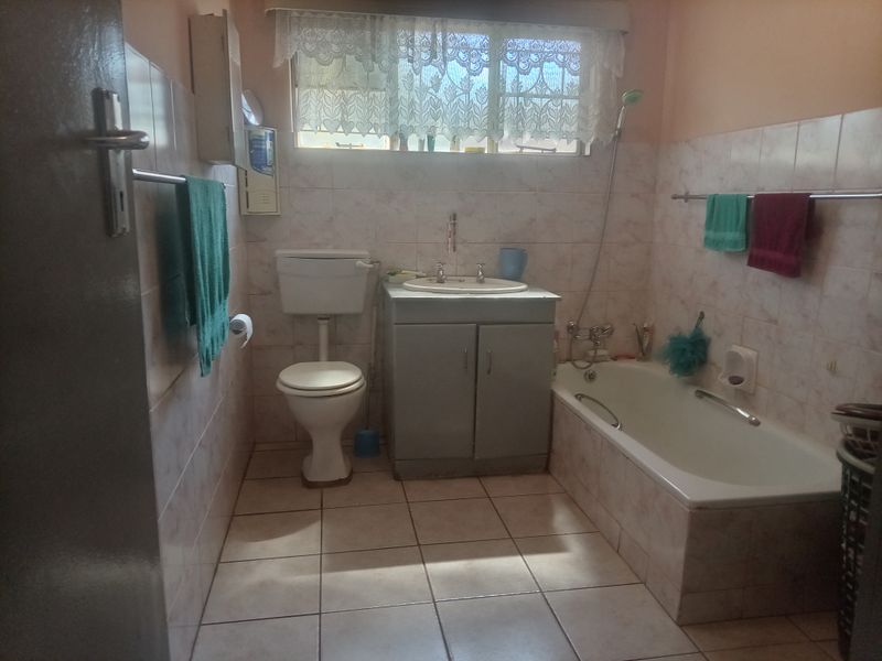 A functional bathroom featuring a built-in vanity, standard toilet, and bathtub with wall-to-floor tiling, offering potential for a modern renovation.