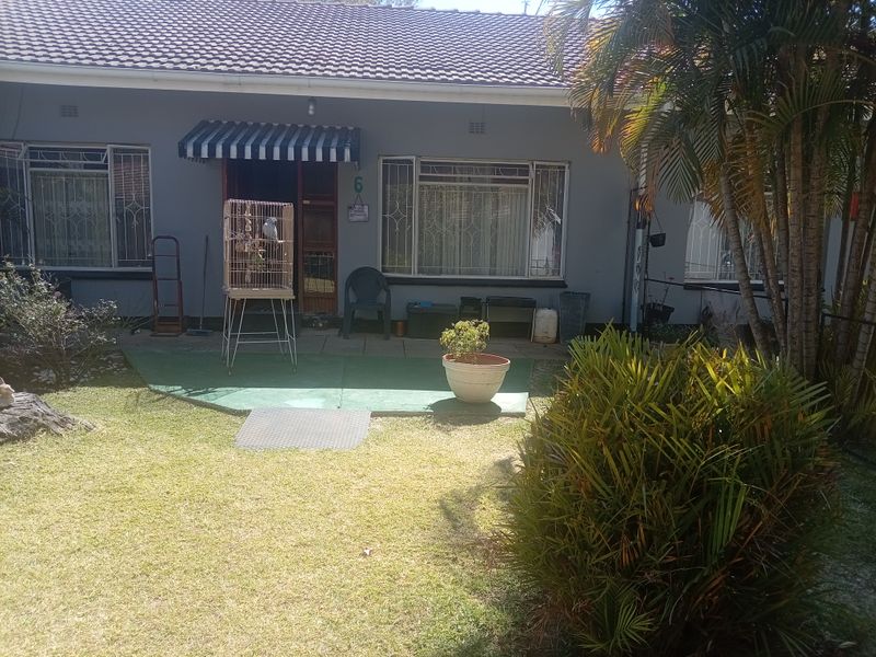 Front view of a townhouse featuring a tiled roof, security bars on windows, a small paved patio area, and a front lawn.