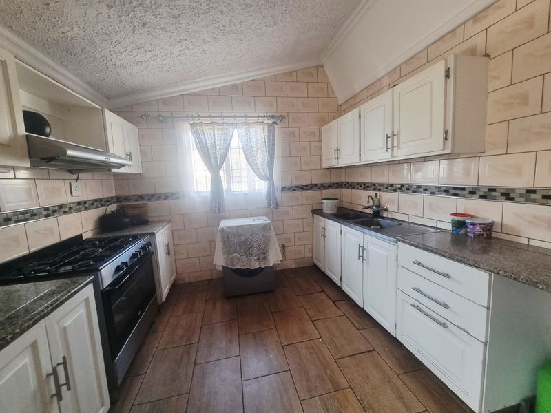 A functional kitchen featuring white cabinetry, granite countertops, a gas stove with extractor fan, and tiled flooring with a neutral tiled splashback.