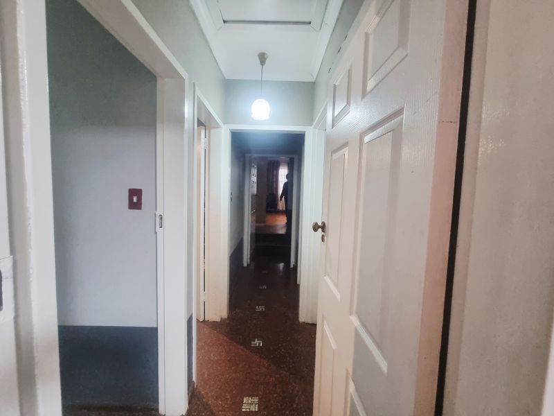 A functional hallway featuring traditional terrazzo flooring, panelled doors, and overhead pendant lighting, connecting multiple rooms within the home.