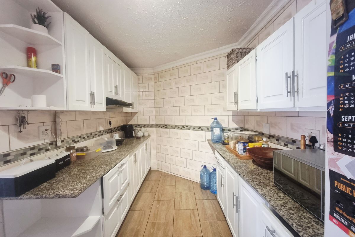 A functional galley-style kitchen featuring white cabinetry, granite countertops, a tiled backsplash, and wood-look floor tiles.