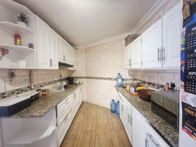 A functional galley-style kitchen featuring white cabinetry, granite countertops, a tiled backsplash, and wood-look floor tiles.