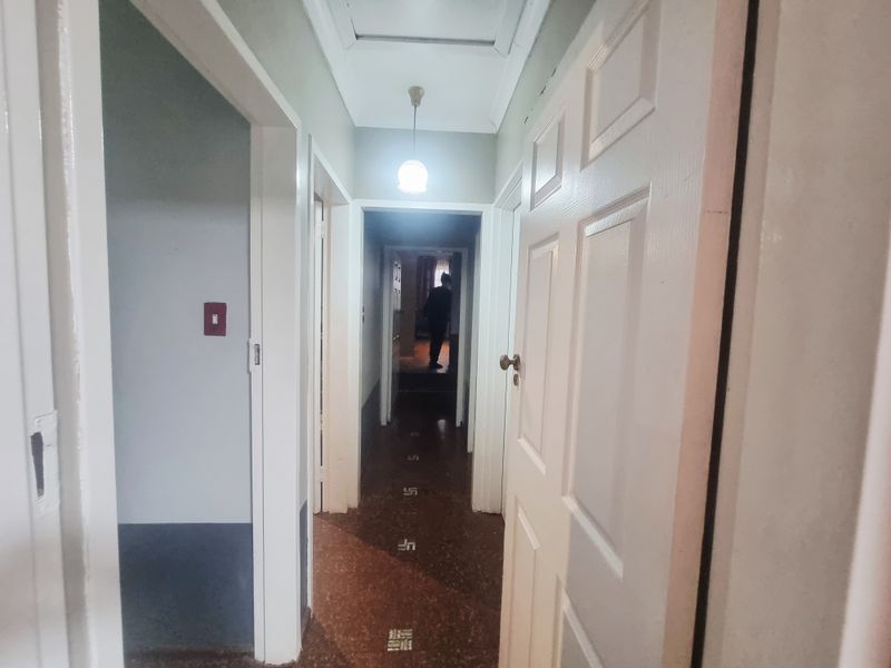 A narrow residential hallway featuring traditional terrazzo flooring, a ceiling access hatch, and a central pendant light fixture.