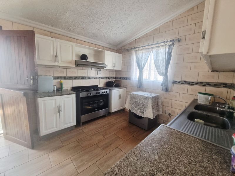 A functional kitchen featuring built-in cabinetry, a gas stove with extractor fan, granite countertops, and a double sink with tiled backsplash.