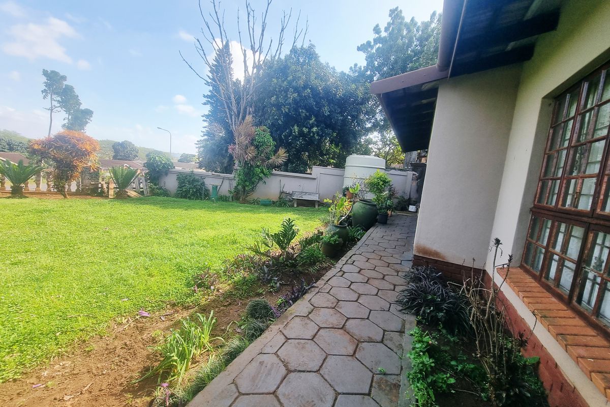 A view of the rear garden featuring a paved walkway, established lawn, and perimeter walling with a water storage tank.