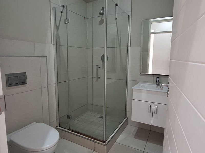 A clean, modern bathroom featuring a glass-enclosed shower, wall-mounted toilet, and a vanity unit with a basin.