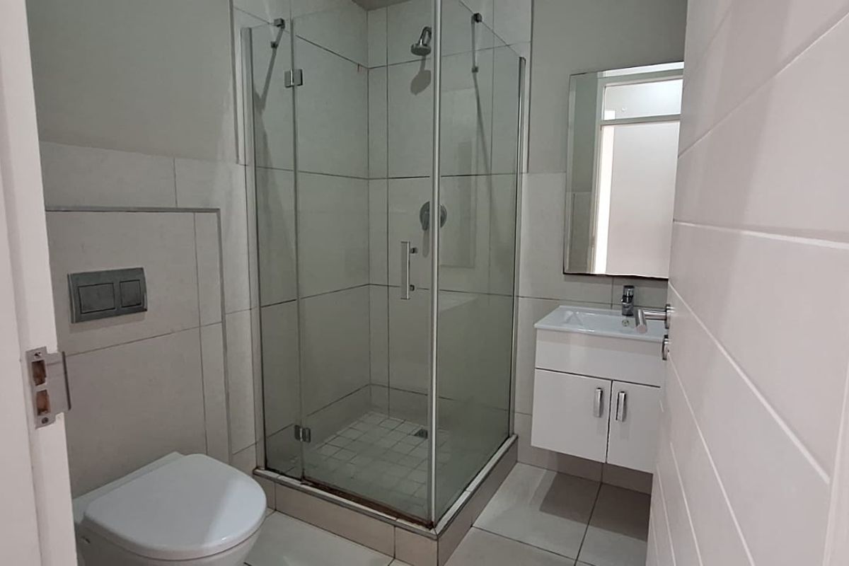 A clean, modern bathroom featuring a glass-enclosed shower, wall-mounted toilet, and a vanity unit with a basin.