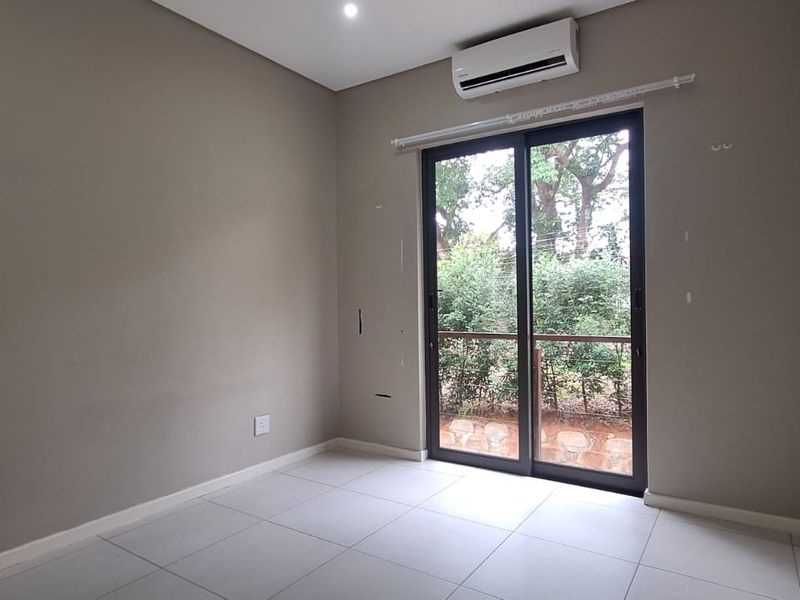 An empty bedroom featuring tiled flooring, a wall-mounted air conditioning unit, and a sliding glass door providing access to the exterior.