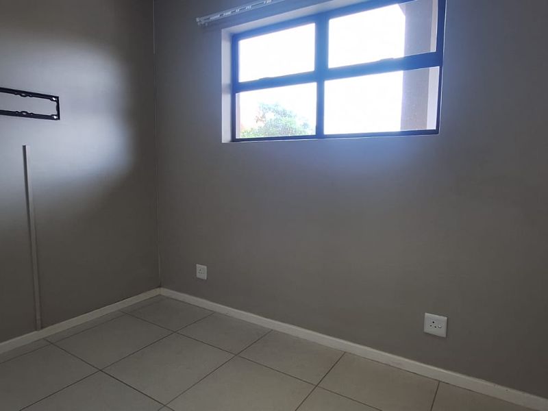 A clean, empty bedroom featuring neutral grey walls, tiled flooring, and a horizontal window, providing a versatile space ready for personalization.