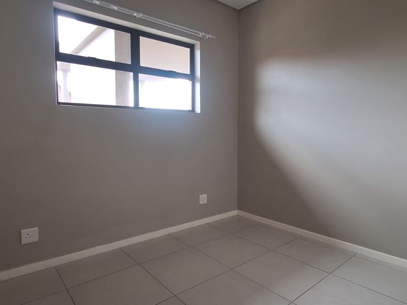 A clean, empty bedroom featuring neutral wall paint, tiled flooring, and an aluminium-framed window, providing a versatile space ready for personalization.