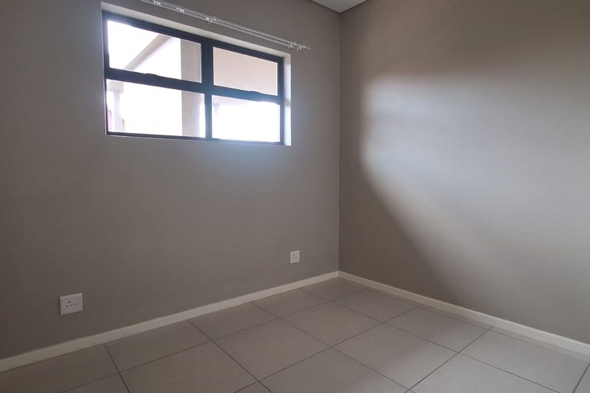 A clean, empty bedroom featuring neutral wall paint, tiled flooring, and an aluminium-framed window, providing a versatile space ready for personalization.
