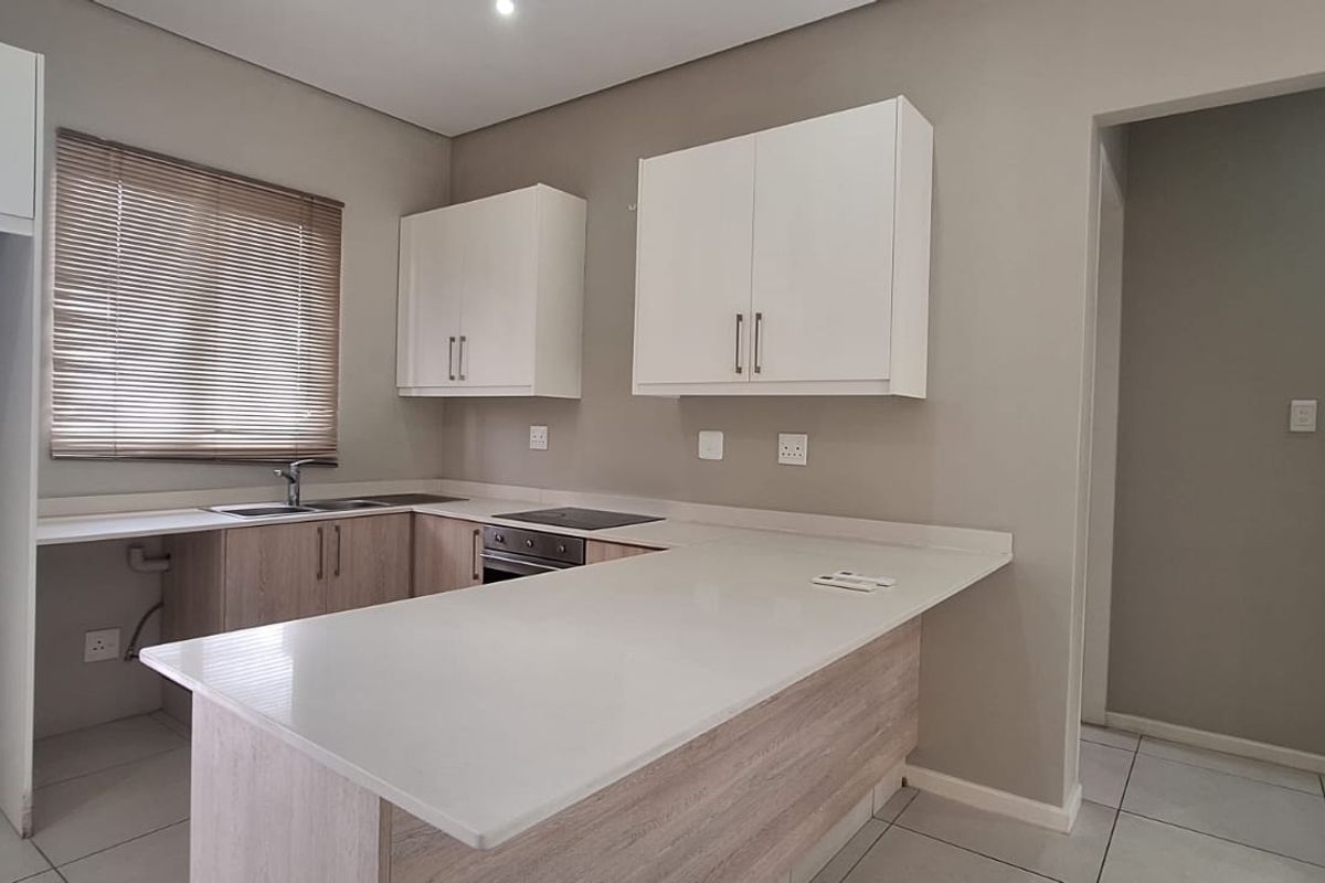 Modern kitchen featuring light wood-tone cabinetry, stone countertops, integrated electric hob and oven, and neutral tiled flooring in an open-plan layout.