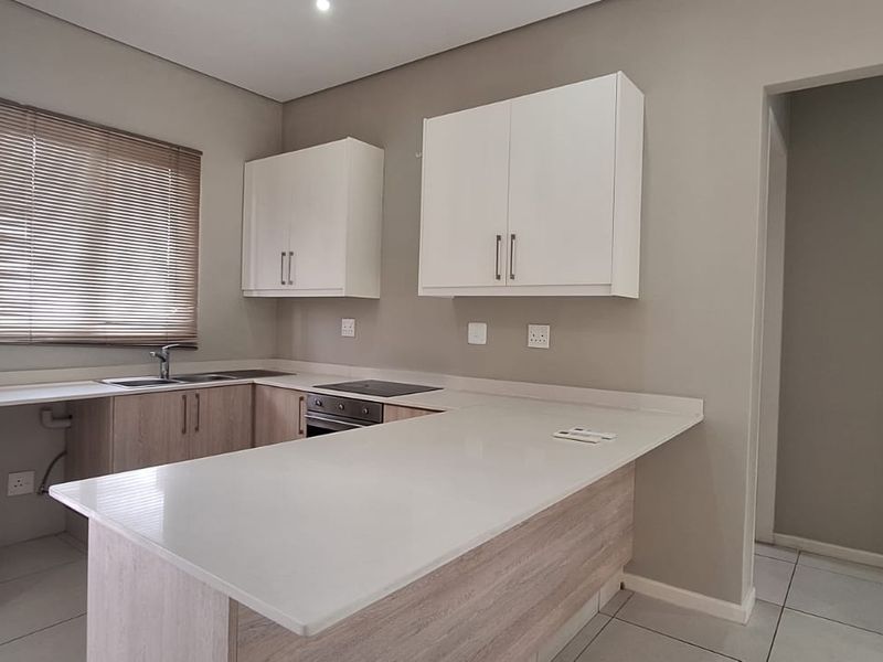Modern kitchen featuring light wood-tone cabinetry, stone countertops, integrated electric hob and oven, and neutral tiled flooring in an open-plan layout.
