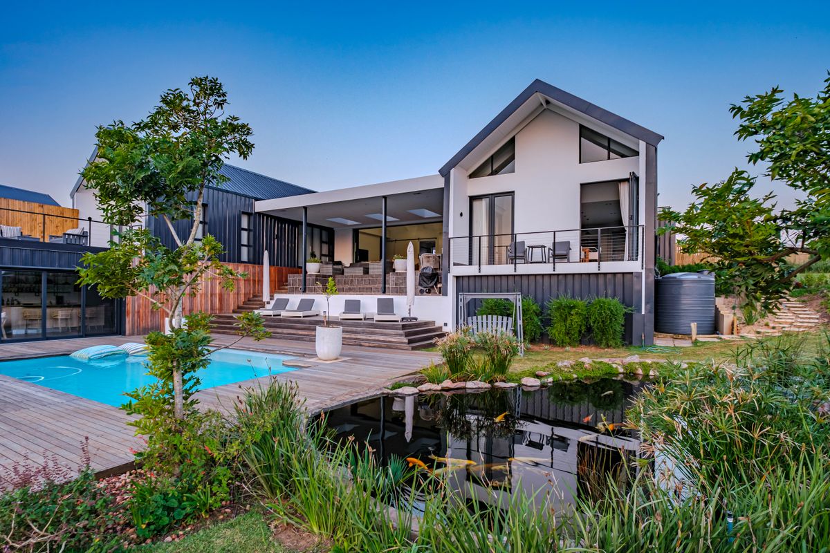 A modern rear exterior featuring a swimming pool, timber decking, a koi pond, and a covered patio area with balcony access.
