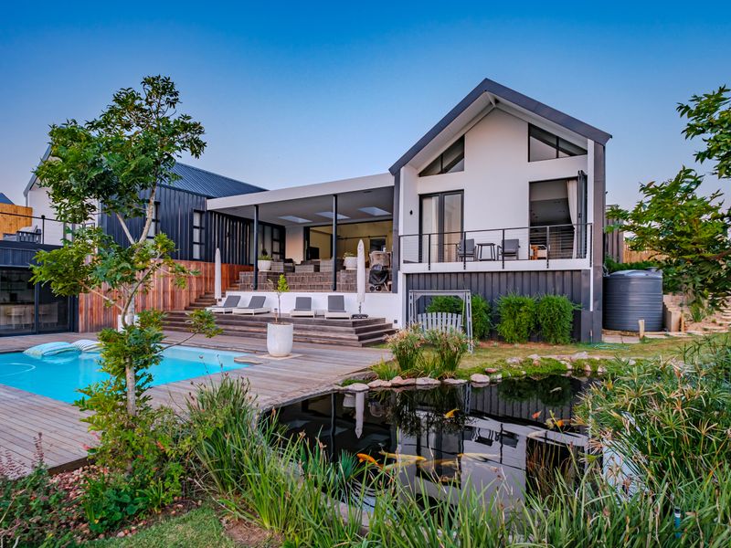 A modern rear exterior featuring a swimming pool, timber decking, a koi pond, and a covered patio area with balcony access.
