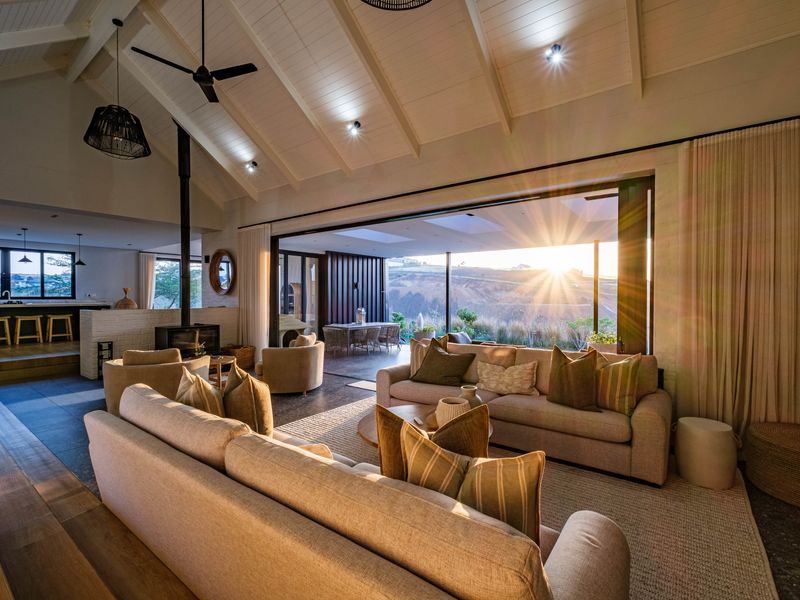 Spacious open-plan living area featuring a vaulted ceiling with exposed rafters, a wood-burning fireplace, and expansive sliding doors opening to a scenic outdoor view.