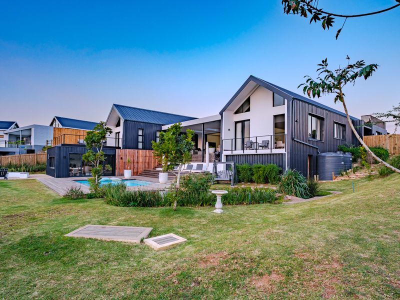 Modern rear exterior view featuring a swimming pool, timber decking, and contemporary architectural design with metal cladding and large glass openings.