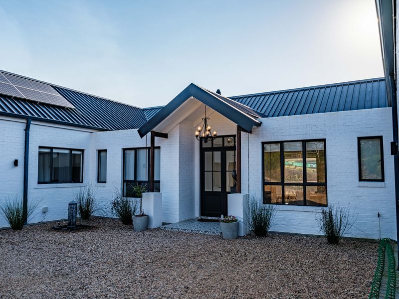 Modern white painted brick home featuring a metal roof, solar panels, and a welcoming covered entrance with large windows.