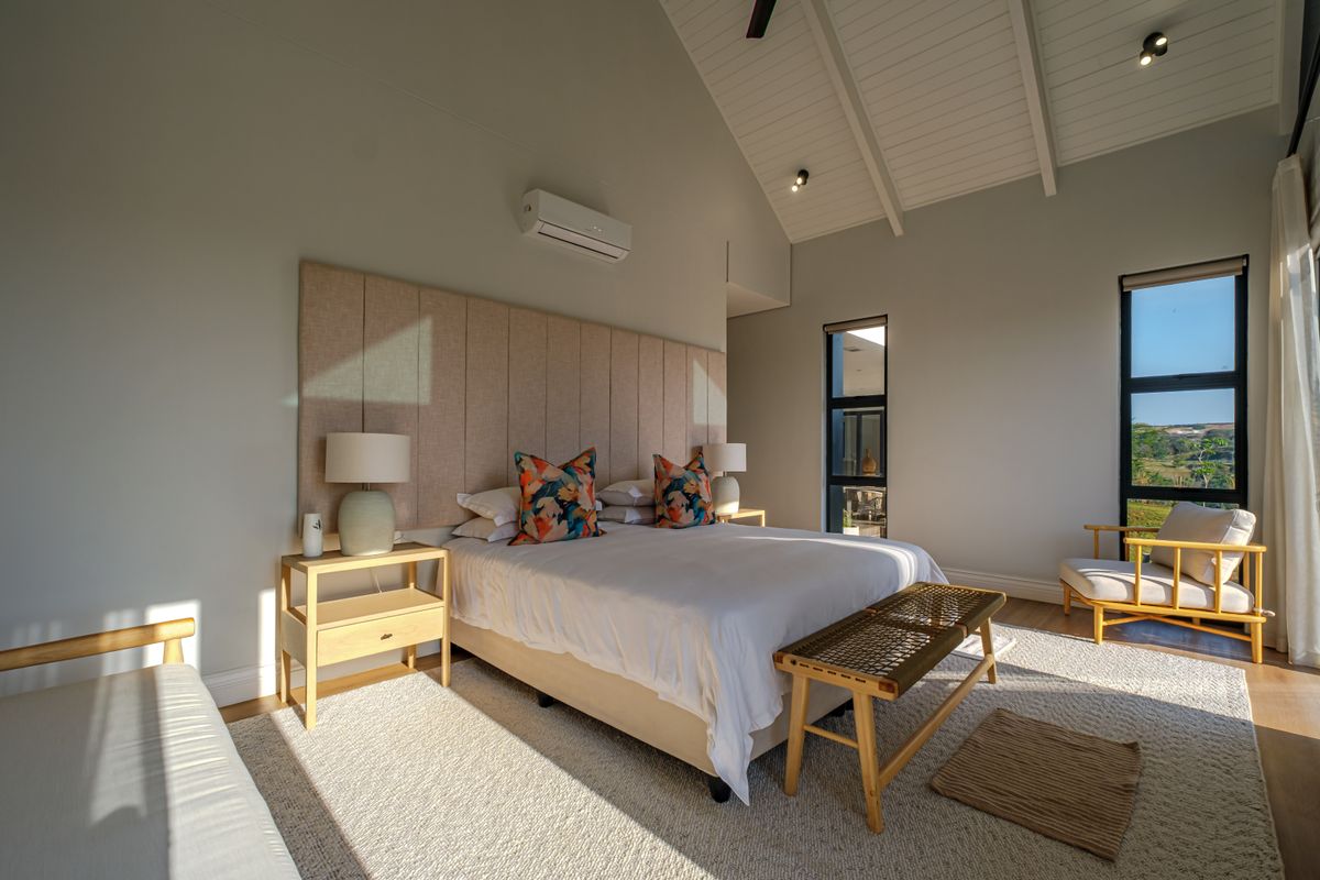 Spacious bedroom featuring a high vaulted ceiling with exposed rafters, large windows for natural light, and a wall-mounted air conditioning unit.