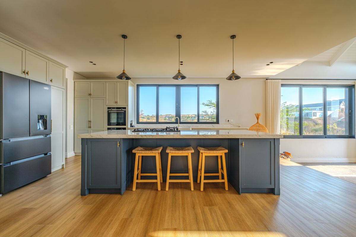 Modern kitchen featuring a large central island with stone countertops, shaker-style cabinetry, built-in oven, gas cooktop, and elegant pendant lighting.