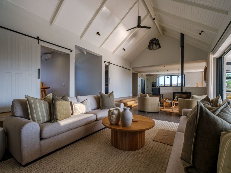Spacious open-plan living area featuring a high vaulted ceiling with exposed rafters, a modern wood-burning fireplace, and seamless flow to the kitchen.