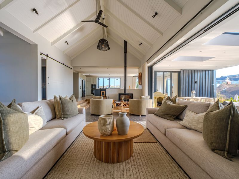 Spacious open-plan living area featuring a vaulted ceiling with exposed beams, a modern freestanding fireplace, and large sliding doors opening to the outdoors.