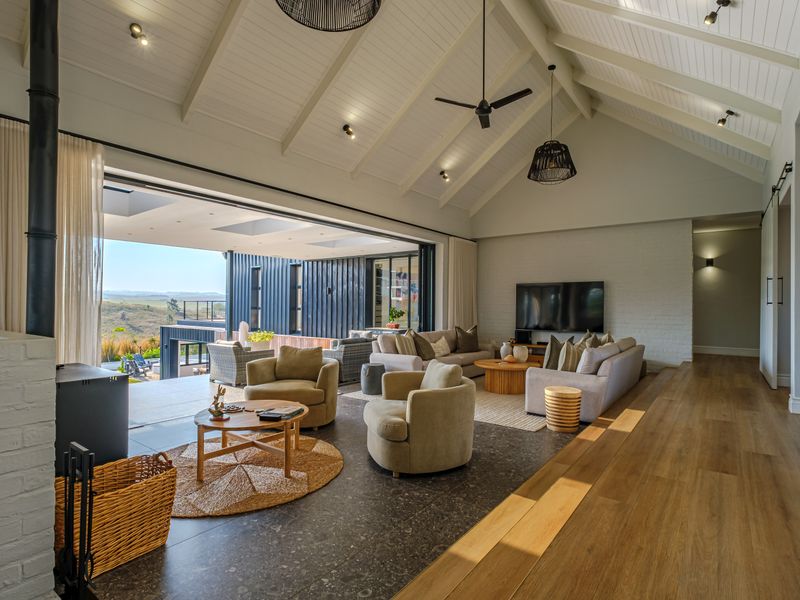 Spacious open-plan living area featuring a vaulted ceiling with exposed beams, a wood-burning fireplace, and seamless indoor-outdoor flow through large sliding glass doors.