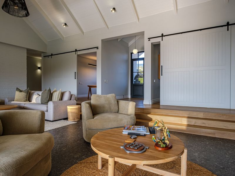 Spacious living area featuring a vaulted ceiling with exposed beams, sliding barn doors, and a split-level design with a mix of stone and timber flooring.