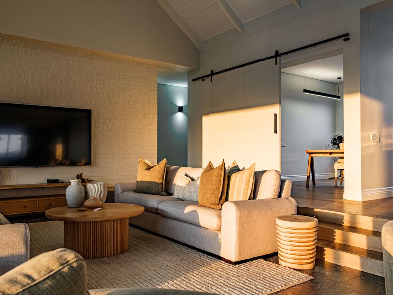 A bright, modern living room featuring a vaulted ceiling, exposed brick wall, and a sliding barn door leading to an adjacent space.