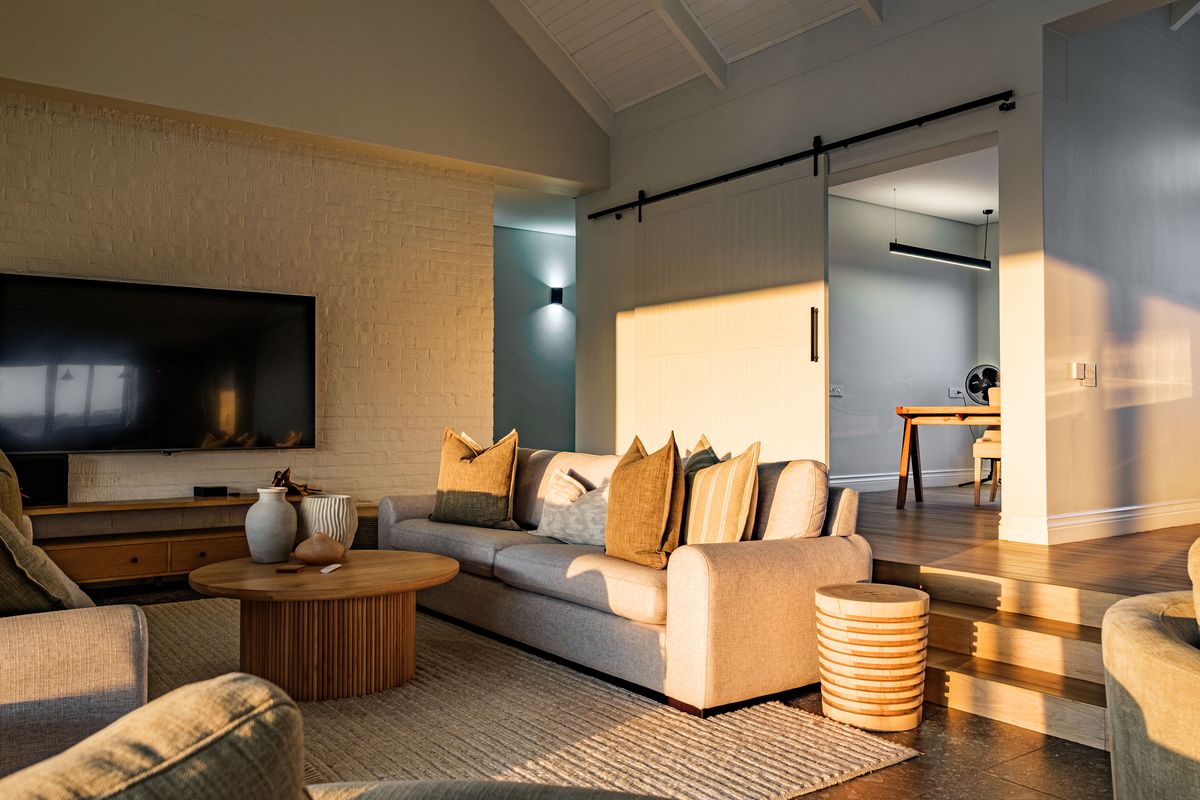 A bright, modern living room featuring a vaulted ceiling, exposed brick wall, and a sliding barn door leading to an adjacent space.