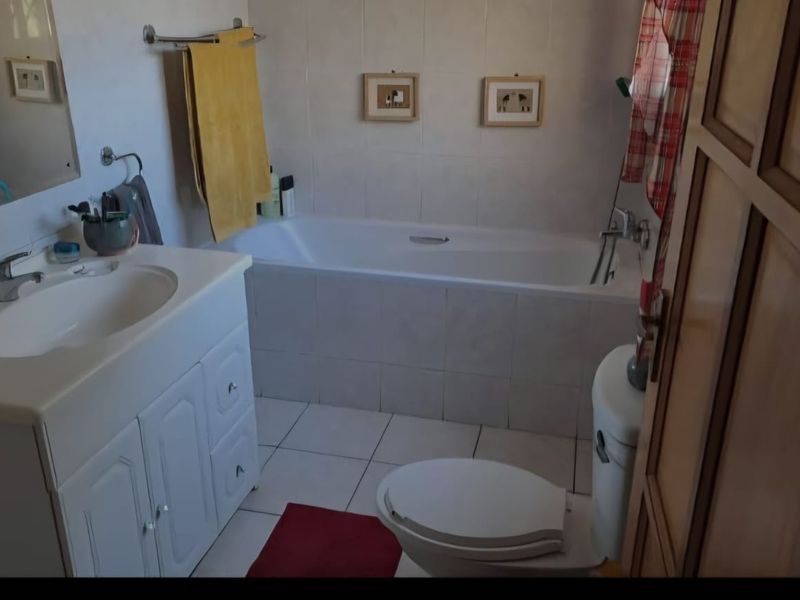 A functional bathroom featuring a built-in vanity, bathtub, and toilet with neutral wall and floor tiling.