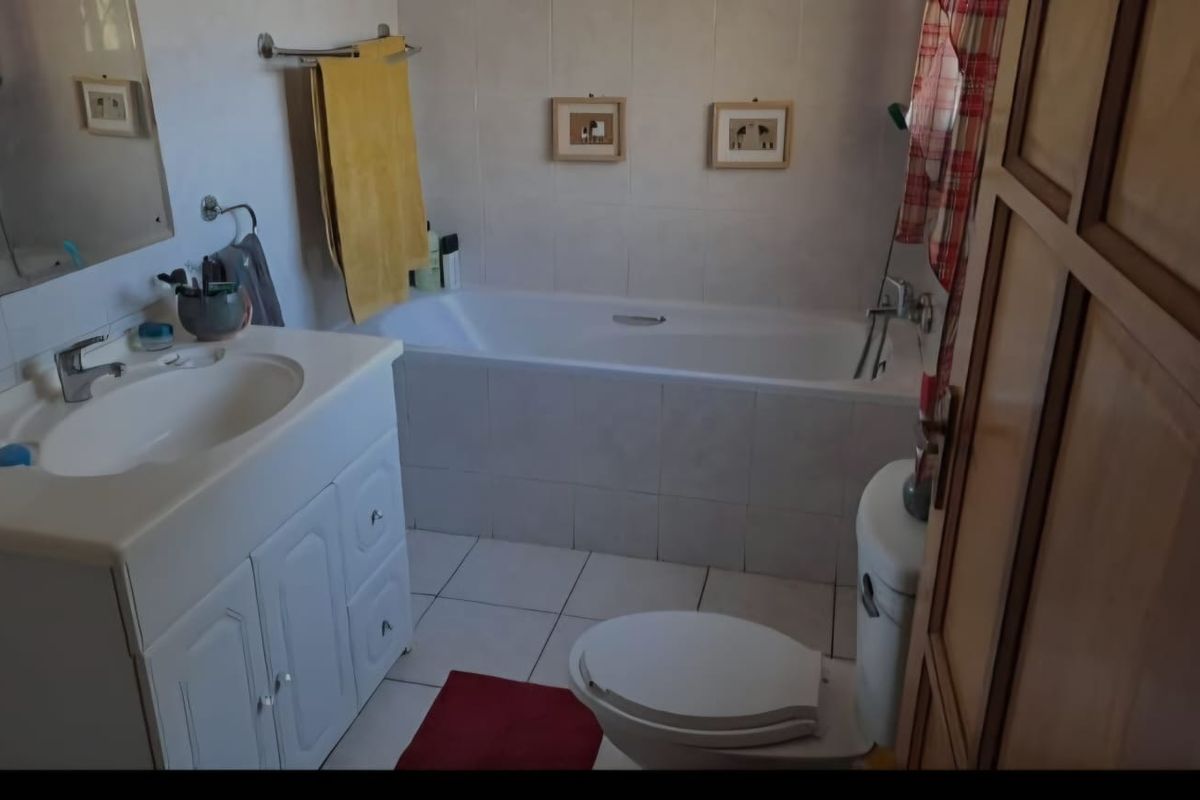 A functional bathroom featuring a built-in vanity, bathtub, and toilet with neutral wall and floor tiling.