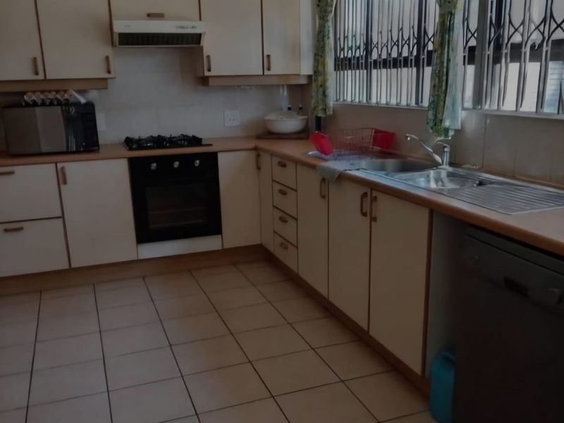 A functional kitchen featuring built-in cabinetry, laminate countertops, a stainless steel sink, and integrated cooking appliances with tiled flooring throughout.
