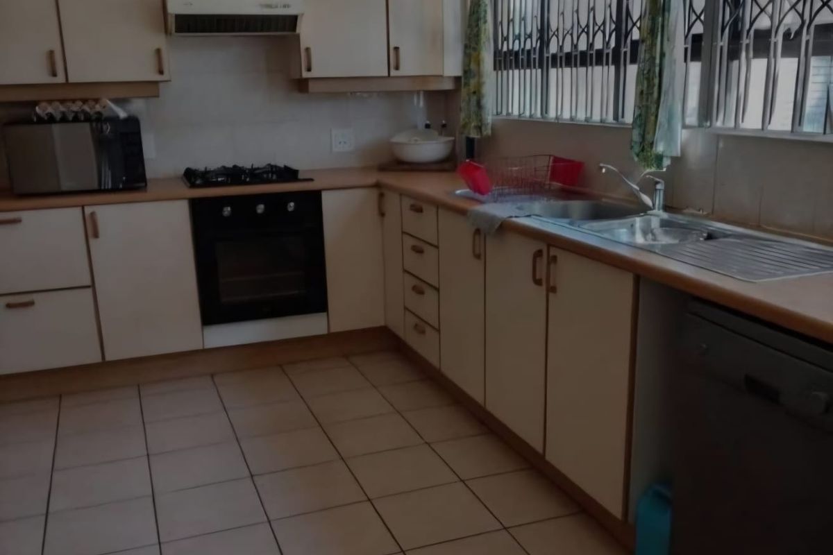 A functional kitchen featuring built-in cabinetry, laminate countertops, a stainless steel sink, and integrated cooking appliances with tiled flooring throughout.