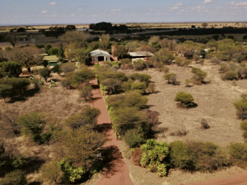Aerial view of a rural small holding property featuring a long dirt driveway, natural vegetation, and multiple outbuildings set within a vast landscape.
