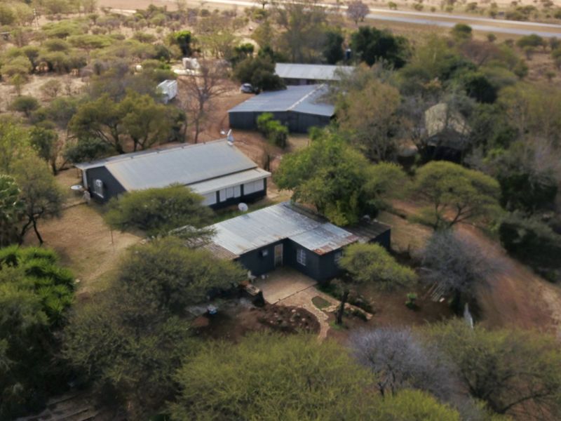 Aerial view of a small holding property featuring multiple structures with corrugated metal roofs, set within a rural landscape with mature trees.